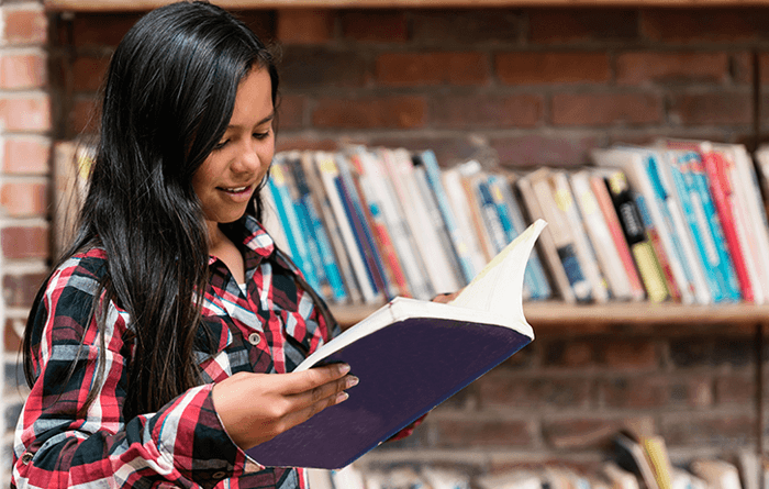 Female student reading book in library.